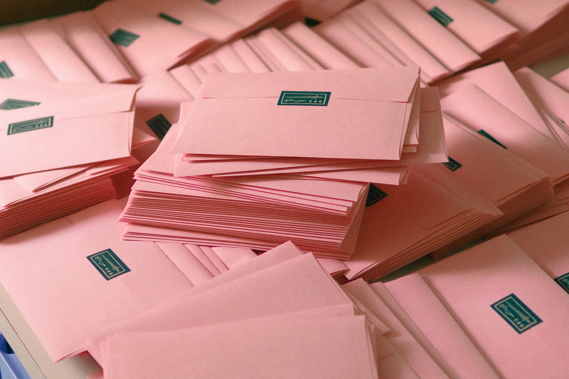 Stacks of soft pink envelopes sealed with dark teal stickers, ready for mailing