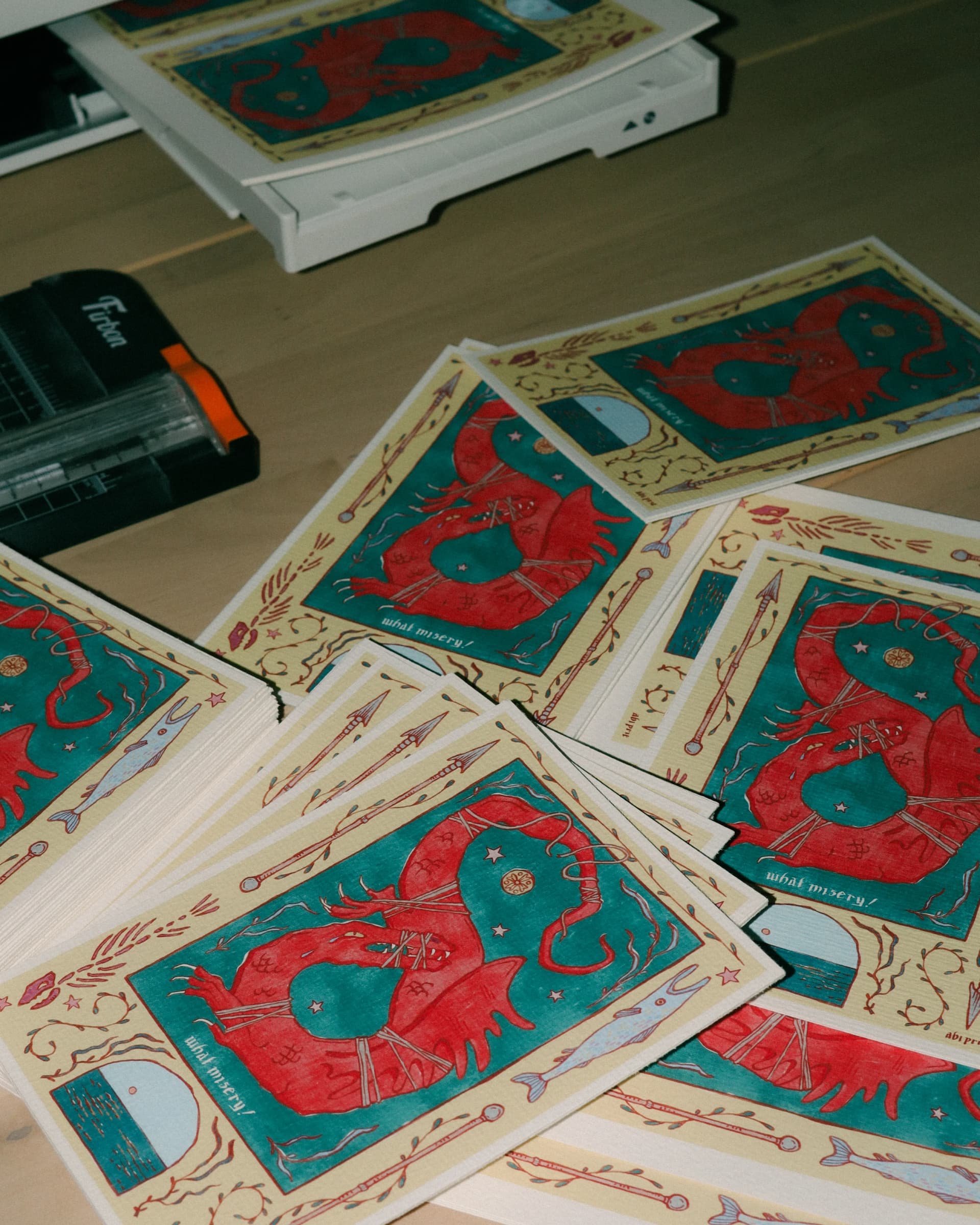 Studio desk covered with copies of a red dragon print titled what misery!