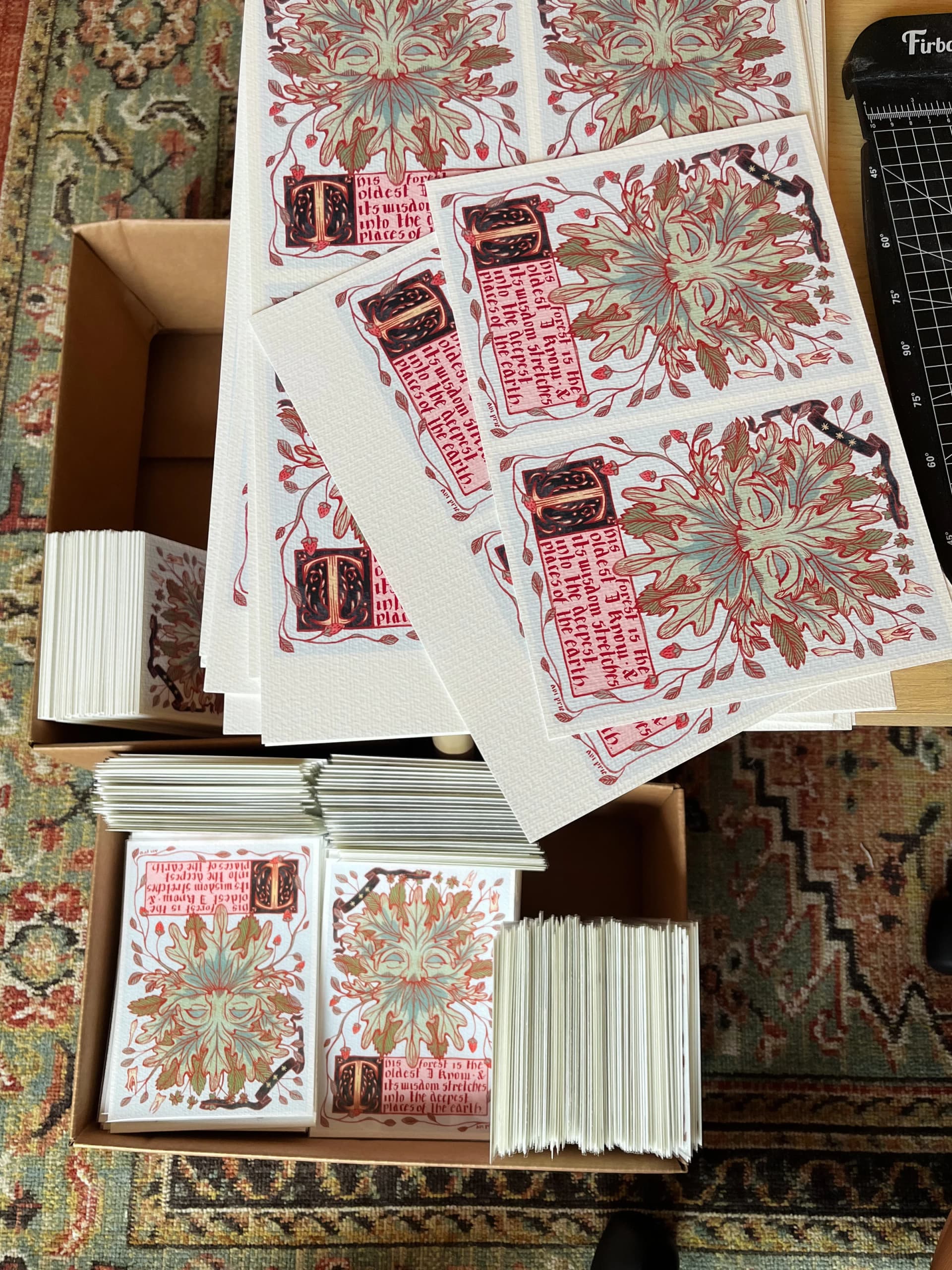Stacks of Green Man oak-leaf prints in cardboard boxes on a patterned rug